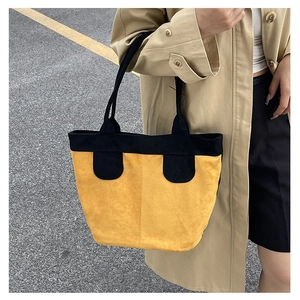 Detail of a large suede tote bag in yellow and black, worn over the shoulder by a model
