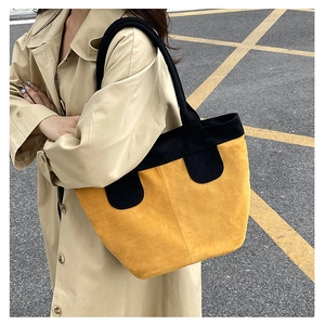 Detail of a large contrast color tote bag made of mustard yellow suede with black handles