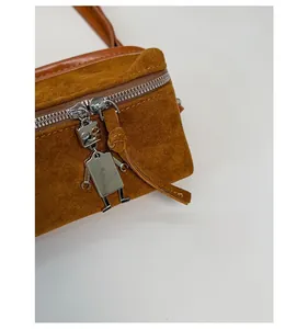 Detailed macro view of a silver robot-shaped metal zipper puller on a brown suede bag
