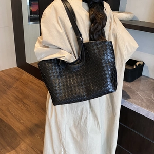 Close-up of black woven leather tote bag showing intricate checkered pattern and shoulder strap