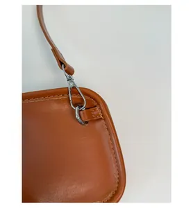 Close-up of brown leather handbag featuring silver metal lobster clasp and stitching
