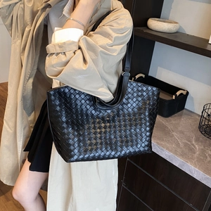 Detail of a large black woven tote bag with leather handles shown in a lifestyle setting