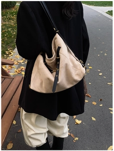 Detail of a beige suede tote bag with black leather straps on a park bench background