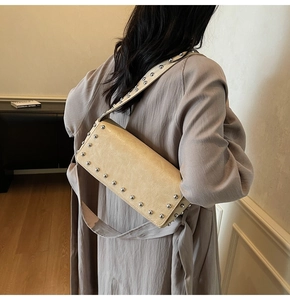 Vue latérale du sac baguette beige à rivets porté par un mannequin en intérieur épuré