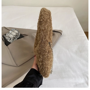 Detail of soft brown plush handbag with silver metal chain on white bedding