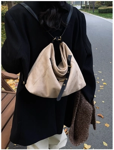 Close-up of beige suede hobo bag with black leather straps on a walking model outdoors