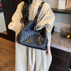 Close-up of a large black woven leather tote bag shown on model with shoulder strap