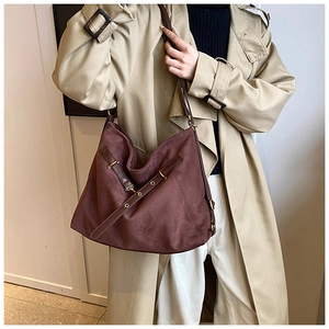 Detailed close-up of dark brown suede hobo bag with leather strap worn by a model in a trench coat