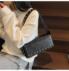 Gros plan du sac baguette en cuir noir orné de rivets argentés et large bandoulière mode