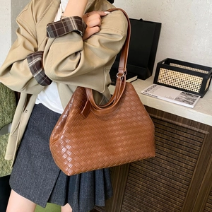 Detail of brown woven tote bag featuring leather texture and adjustable shoulder strap