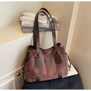 Detail of a dark brown suede tote bag with leather straps and metallic rivets