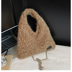 Close-up of brown plush triangular handbag with silver chain strap on white desk