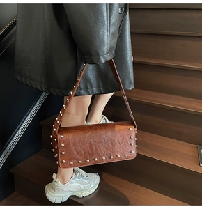 Détail du sac en cuir vintage marron avec rivets métalliques sur escalier en bois