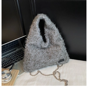 Detail of gray plush tote bag with silver chain and leather tag on a desk