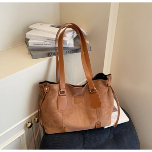 Detail of a large brown suede tote bag with smooth leather straps on a dark chair