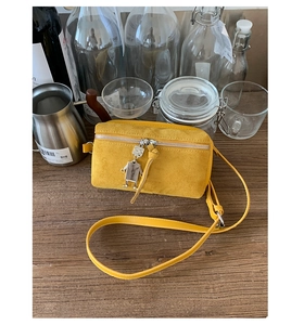 Detail of yellow suede camera bag with silver robot charm on wooden tabletop