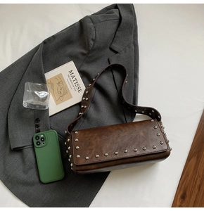 Détail d'un sac baguette en cuir marron à rivets, stylisé avec un blazer gris chic