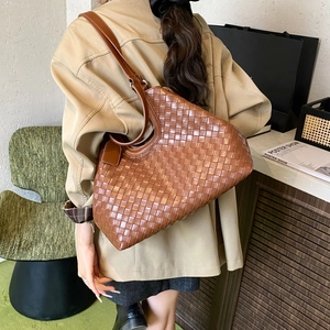 Detail view of large brown woven leather tote bag worn by model in a cozy interior
