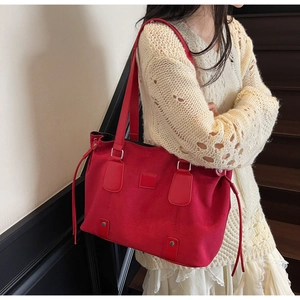 Detail of red large tote bag in matte suede texture carried by a model on a shoulder