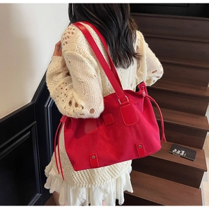 Detail of red matte tote bag featuring leather straps, metal rivets, and drawstring side