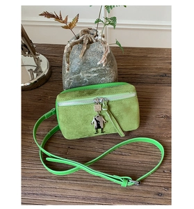 Detail of green suede crossbody bag with robot charm on rustic wooden surface