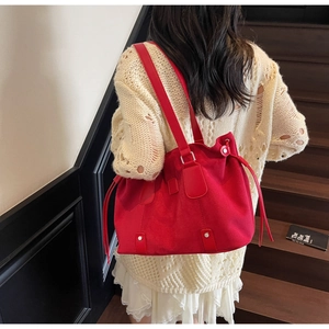 Detail of red matte shoulder bag with side drawstring and metal studs worn by model