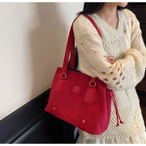 Detail of red matte tote bag with silver studs and long leather handles on model