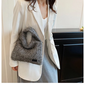 Close-up of grey plush shoulder bag with silver metal chain on a white blazer outfit