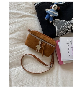 Detail of brown suede crossbody bag featuring a unique silver metal robot charm and zipper