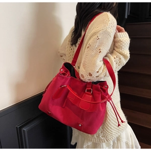 Detail of red suede bucket bag showing drawstring closure and crossbody strap on shoulder