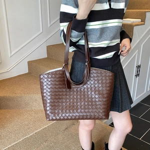 Detail of dark brown large tote bag featuring classic woven texture and leather straps