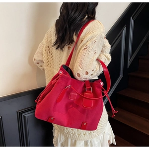 Detail view of large red suede tote bag with drawstring closure on model's shoulder