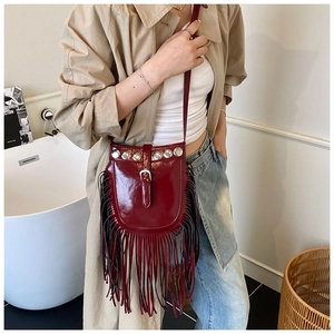 Detail of burgundy patent leather saddle bag featuring fringe and silver rivets
