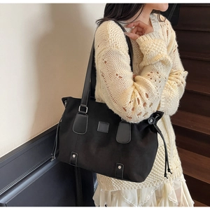Detail of black tote bag featuring leather stitching and silver rivets on the side