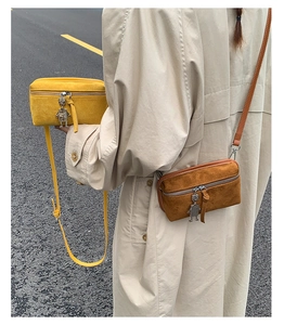 Detail of yellow and brown crossbody bags with unique metal robot charms on a city street