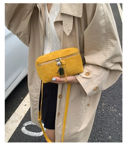 Detailed shot of yellow suede crossbody bag with robot charm in a street style setting