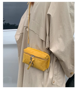Detail of yellow suede mini crossbody bag with a robot zipper charm on a beige trench coat
