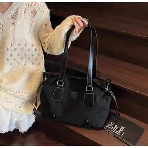 Detail of a black high-capacity tote bag with side drawstrings and leather shoulder strap