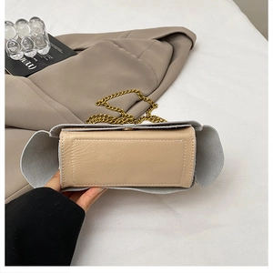 Detail of oatmeal leather envelope bag with gold chain strap on a beige suit background