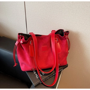 Detail of red suede tote bag showing smooth leather straps and metal base rivets