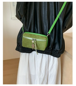 Macro shot of green faux suede crossbody bag with zipper and silver person charm