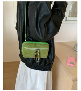 Close-up of a vibrant green suede crossbody bag featuring a unique metal doll pendant