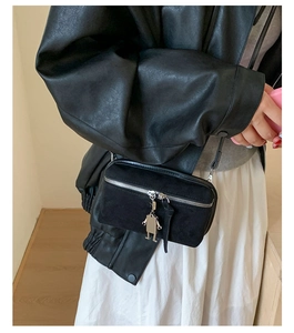Detail of black suede crossbody box bag with silver zipper and robot metal pendant accessory