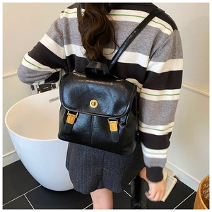 Model wearing a vintage black PU leather backpack with gold buckles in a bright indoor setting