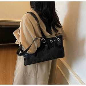 Gros plan d'un sac porté épaule noir vintage avec œillets argentés sur un trench