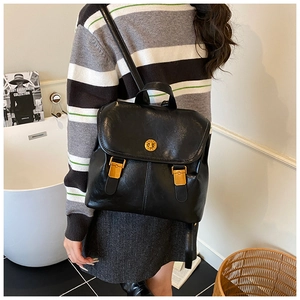 Detail of a vintage black leather backpack with a golden round metal buckle in a home setting