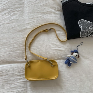 Flat lay of a yellow suede crossbody bag with adjustable strap and silver hardware on bed