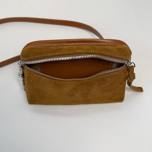 Detail view of brown suede crossbody bag showing the open front zipper pocket and texture
