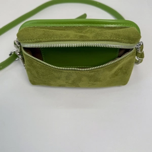 Detail view of the green suede crossbody bag featuring smooth leather edges and silver zipper