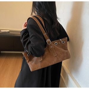 Détail d'un sac cabas en cuir marron avec œillets métalliques et bandoulière à boucle